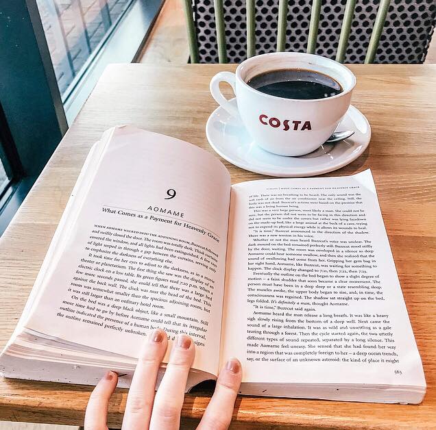 Image is of an open book on a table in Costa Coffee, along with a mug of black coffee